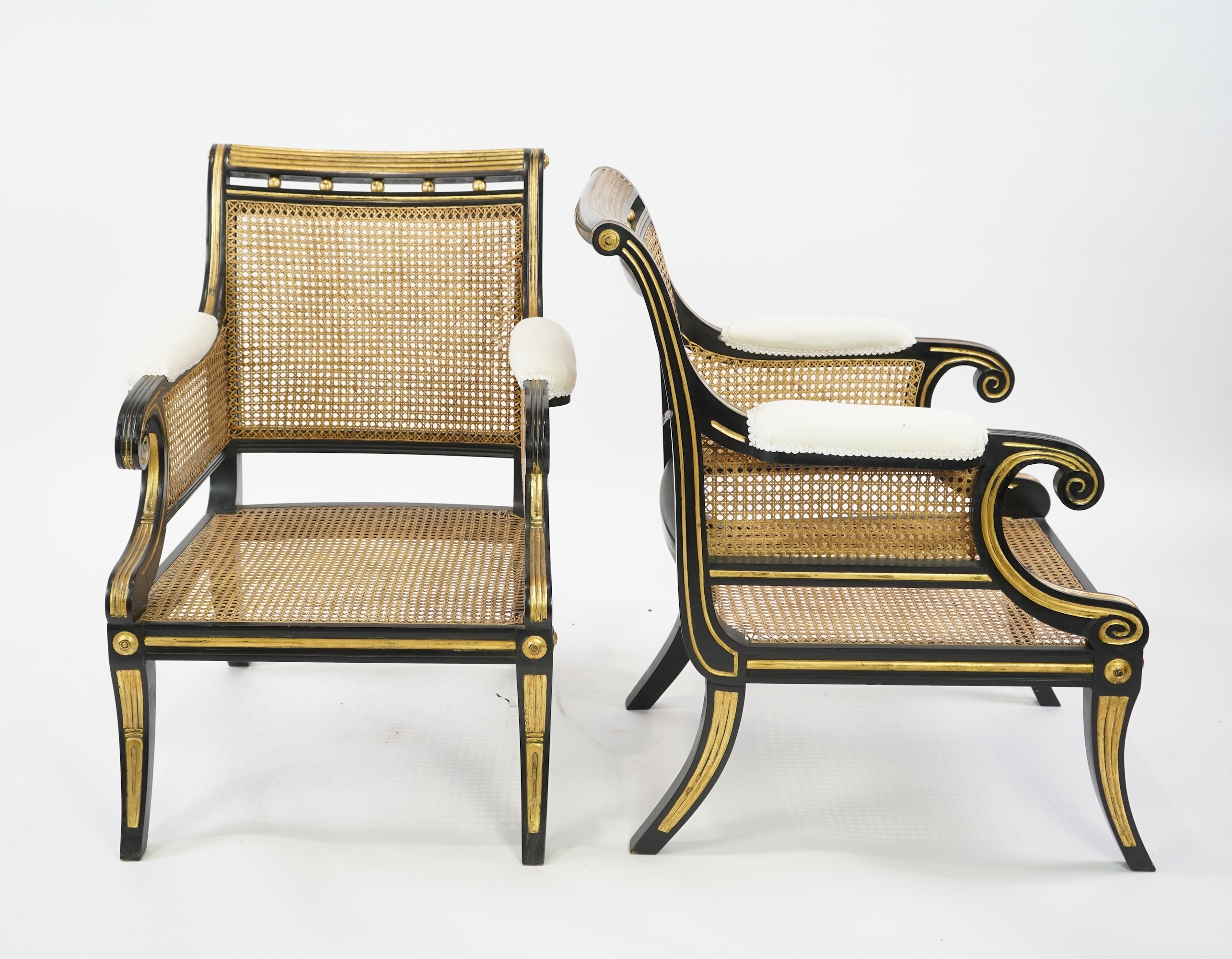 A pair of Regency style ebonised, parcel gilt caned bergere elbow chairs